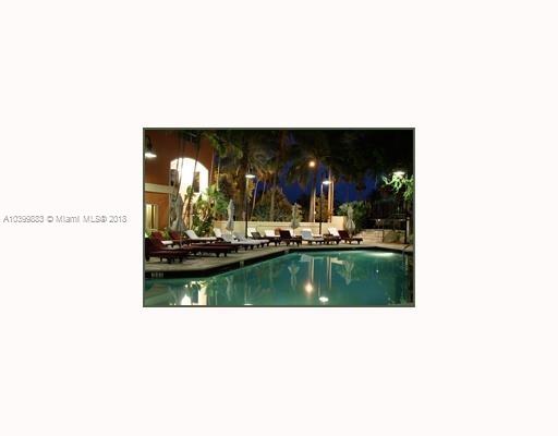 Evening view of a swimming pool surrounded by lounge chairs and palm trees.