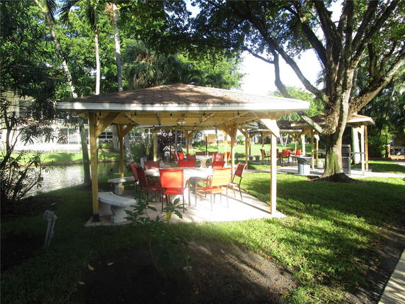 Outdoor seating area under a gazebo with trees surrounding.