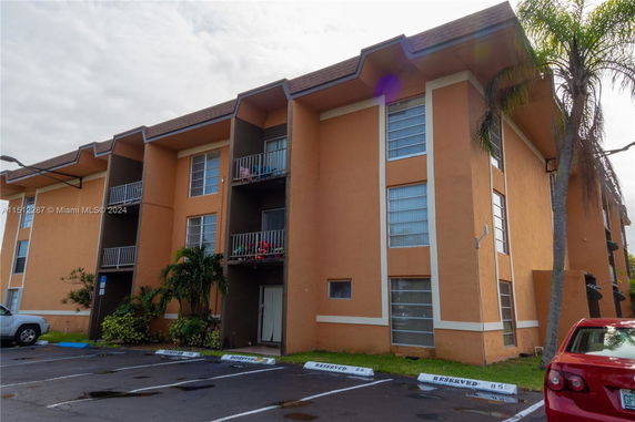 Front view of a multi-story apartment building with a nearby parking area.