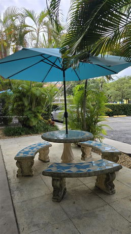 Outdoor seating area with a round table and benches under a large blue umbrella.