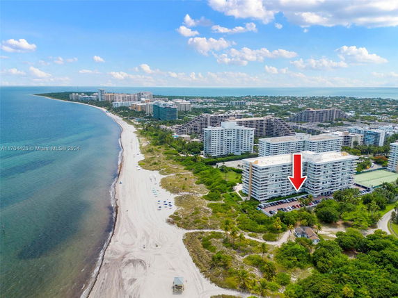 Aerial view of coastal buildings overlooking a sandy beach with surrounding greenery.