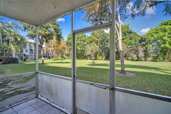 View from a screened porch overlooking a grassy area with trees.