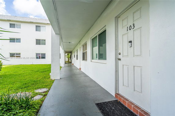 Front view of an apartment complex with white exterior walls and a walkway.