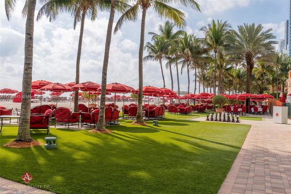 Outdoor seating area with red umbrellas and palm trees.