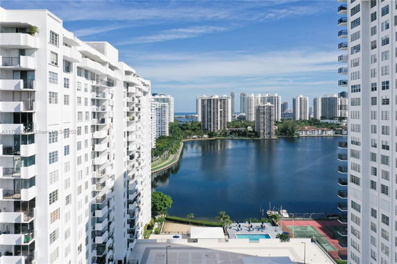 Panoramic view of high-rise buildings overlooking a body of water with tennis courts and a swimming pool in the foreground.