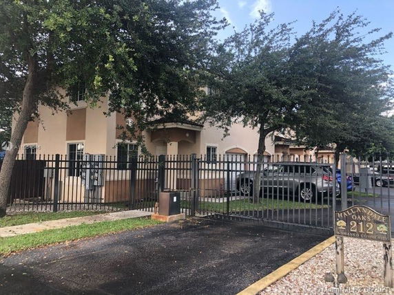 Front view of a multi-story residential building with a gated fence and parking area.
