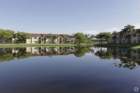 View of buildings reflected in a calm body of water with surrounding greenery.