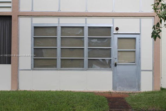 Front view of a building section with a metal door and large windows covered with blinds.