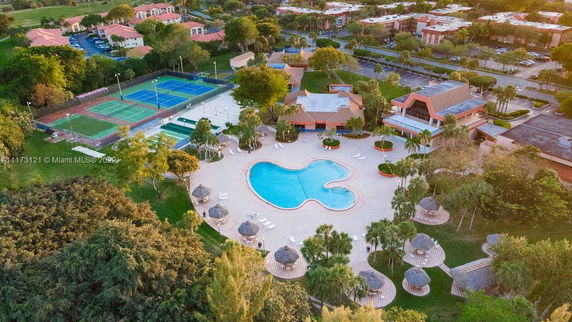 Aerial view of a complex with a swimming pool, tennis courts, and landscaped surroundings.