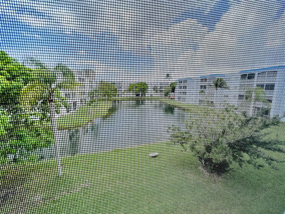 View through a window screen of buildings by a water body and greenery.