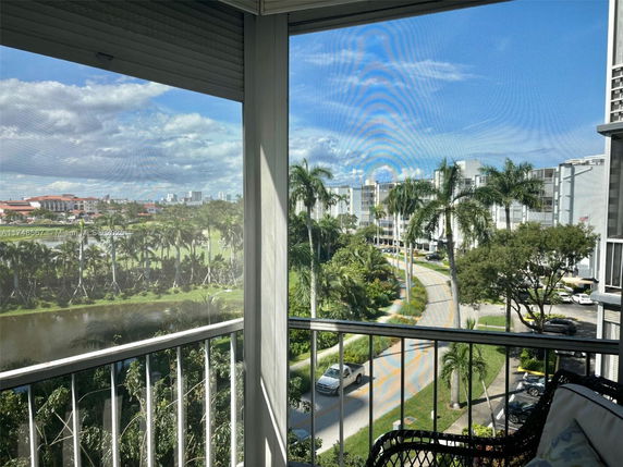 View from a balcony overlooking a lush area with palm trees, buildings, and a road.