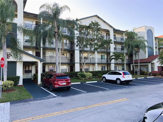 Front view of a multi-story apartment building with balconies and palm trees.