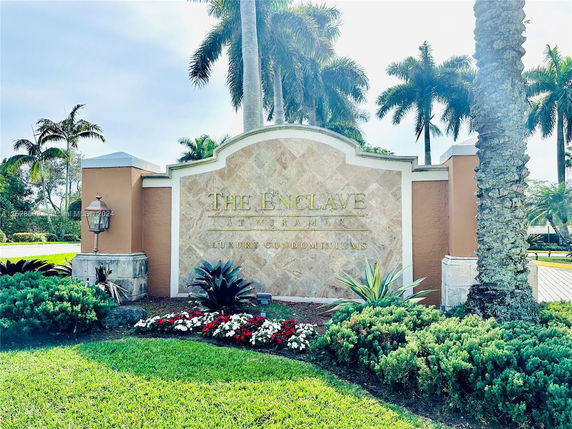 Entrance sign for The Enclave at Miramar Luxury Condominiums with landscaping and palm trees.