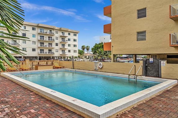 Outdoor swimming pool area beside multi-story residential buildings.