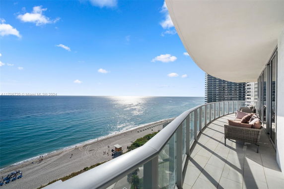Panoramic view from a balcony overlooking the ocean and beach, with a curved glass railing.