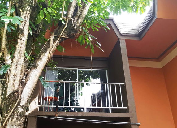 View of a building with an orange exterior and a balcony surrounded by trees.