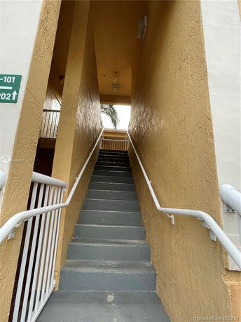 View of an outdoor stairwell with yellow walls leading to an upper level of a building.