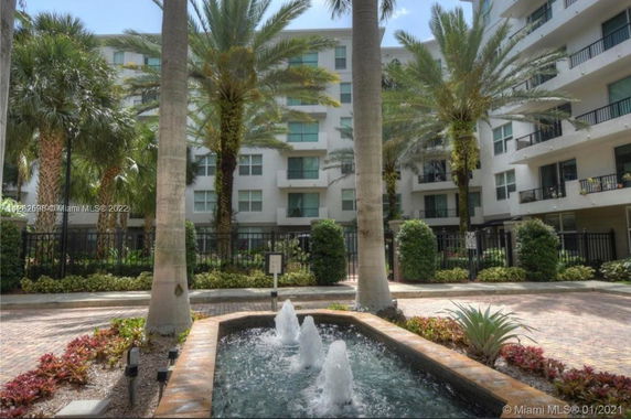 Exterior view of a multi-story residential building with palm trees and a fountain in front.