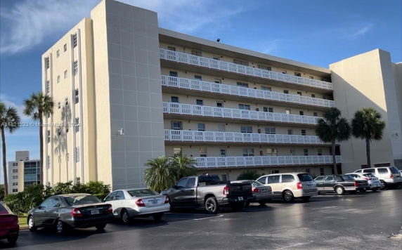 Front view of a multi-story apartment building with balconies, surrounded by palm trees.