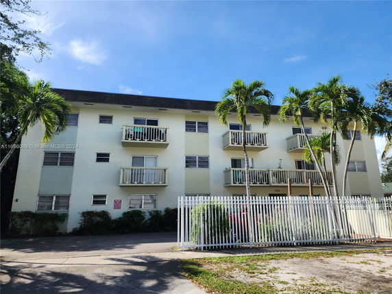 Front view of a multi-story apartment building with balconies and a fenced entrance.