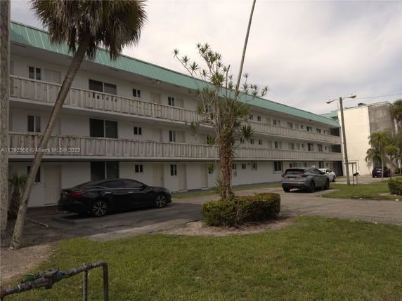 Front view of a multi-story building with a green roof and parking area.
