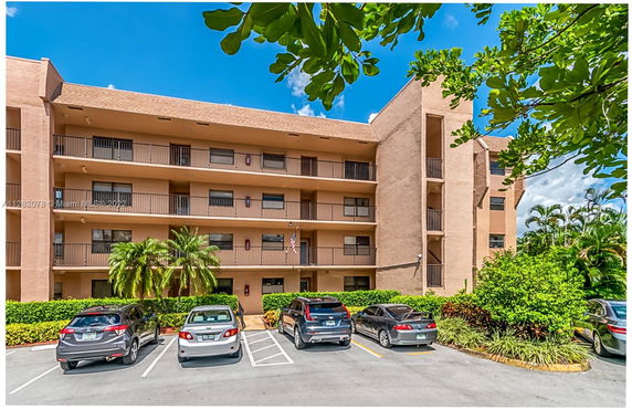 Front view of a multi-story building with balconies and a parking area in front.