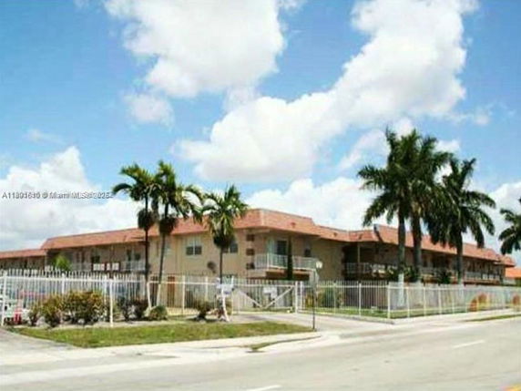 Front view of a two-story residential building with palm trees and a gated entrance.