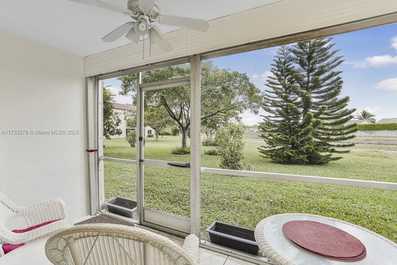 View from a screened patio looking out at a grassy area with trees and a building in the distance.