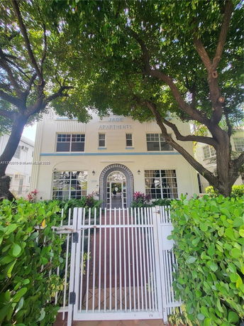 Front view of a two-story apartment building with white facade and gated entrance.