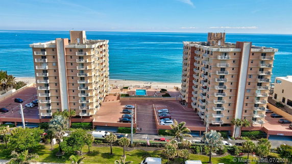View of two multi-story beachfront buildings with balconies and flat rooftops.