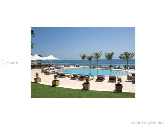 View of a swimming pool area with loungers and palm trees by the ocean.