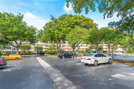 View of a multi-story apartment building with trees and parked cars in the foreground.