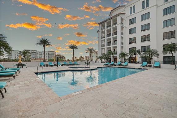View of a multi-story building with a swimming pool and lounge chairs in the foreground.
