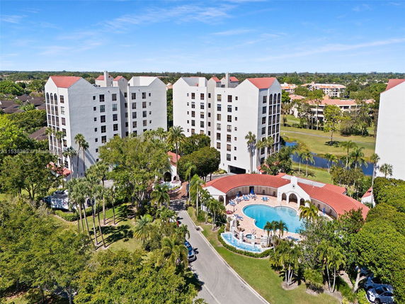 Aerial view of multiple multi-story residential buildings with red-tiled roofs, surrounded by greenery and a pool area in the foreground.