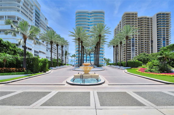 Front view of a luxurious high-rise residential complex with multiple towers and a central driveway with palm trees and a fountain.