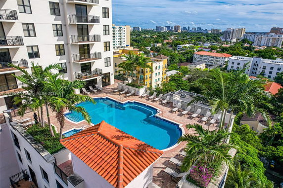 Rooftop view with a swimming pool and lounge chairs on a terrace surrounded by buildings.