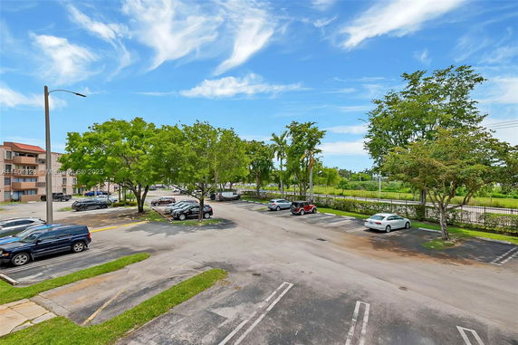 Outdoor parking area with cars parked under trees and a clear blue sky.