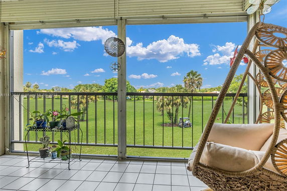 Balcony view with a chair and plants overlooking a green outdoor area with palm trees.