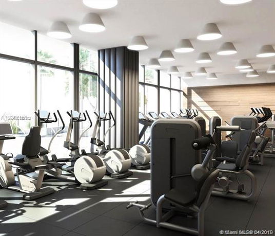 Interior view of a modern gym with exercise equipment and large windows.