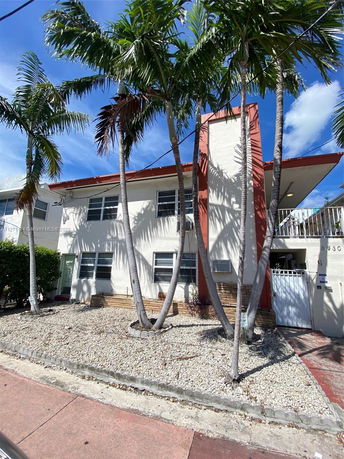 Front view of a two-story building with a distinctive red vertical accent and several palm trees.