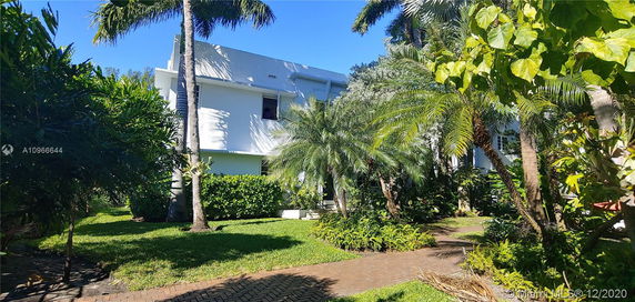Front view of a two-story house surrounded by palm trees and greenery.