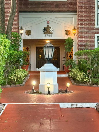 Front view of a building entrance with brick walls, decorative lamps, and a pathway leading to the door.