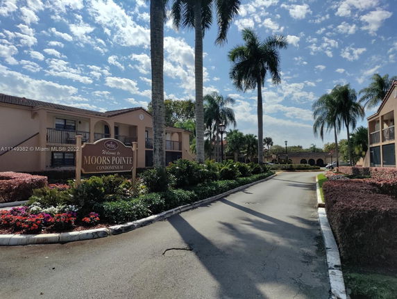 Front view of a condominium complex with palm trees and a sign reading 'Moors Pointe.'