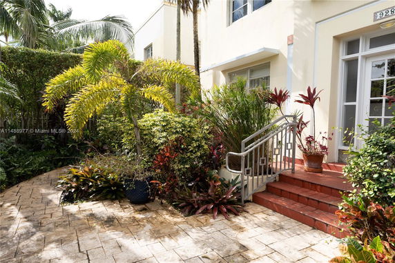 Front view of a house entrance with steps surrounded by tropical plants.