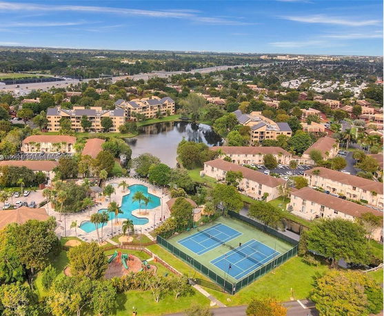 Aerial view of a residential complex with tennis courts, swimming pool, and surrounding greenery.