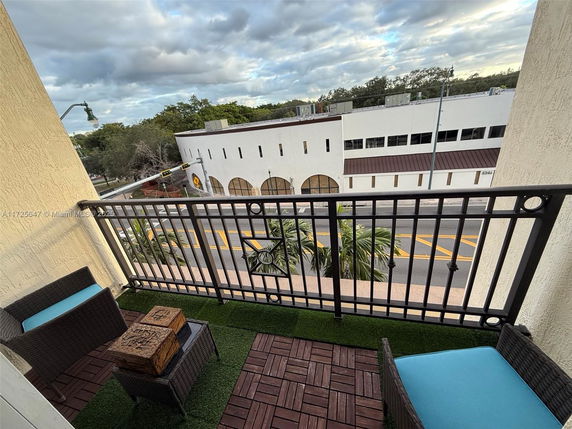 Balcony view overlooking a road and a white building with trees in the background.