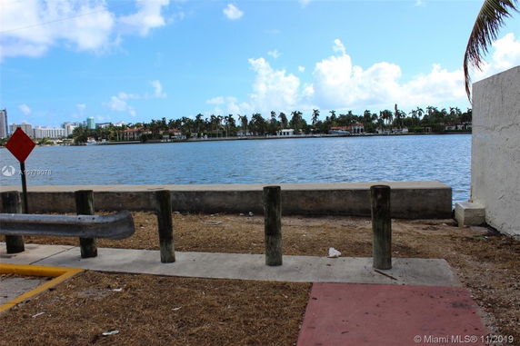 View of a waterfront area with buildings and palm trees in the distance.