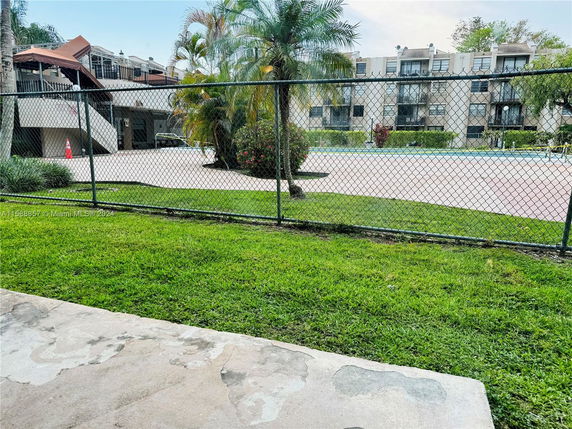 View of an outdoor area with a fenced tennis court near residential buildings.
