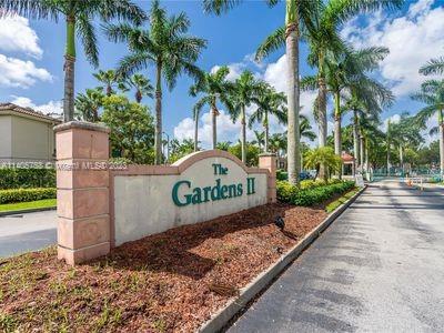 Entrance sign of The Gardens II with palm trees lining the road.