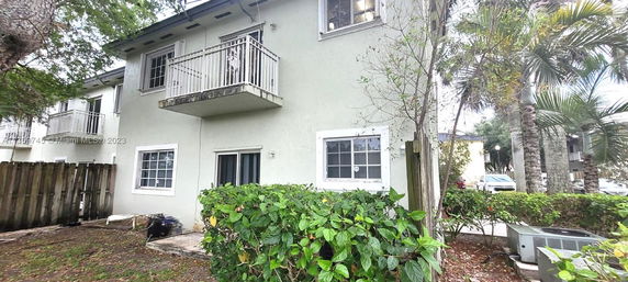Side view of a two-story house with balconies and windows, surrounded by foliage.